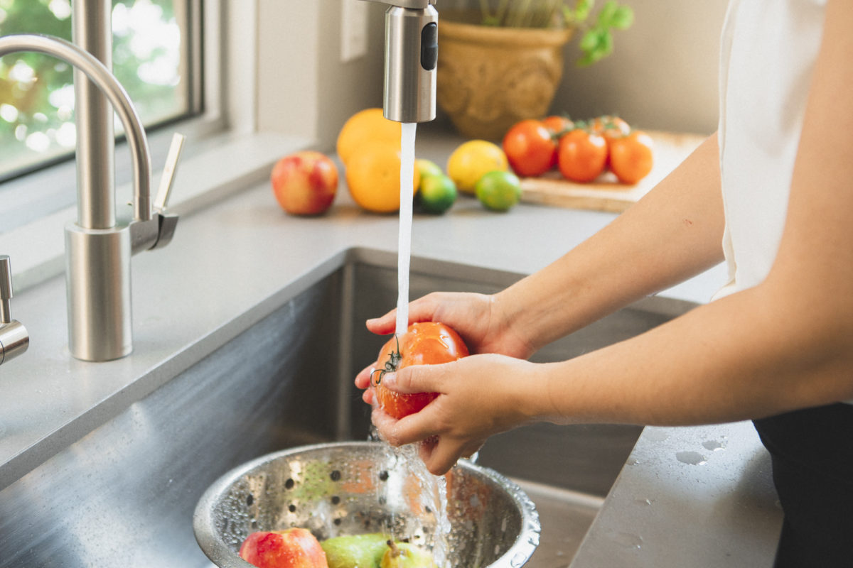 woman washing tomato in sink