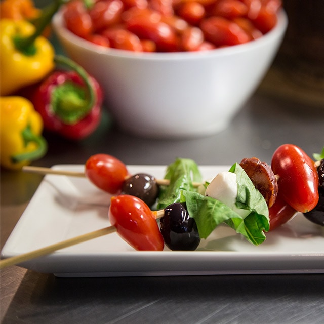 A couple of skewers that contain cherry tomatoes, olives and cheese.