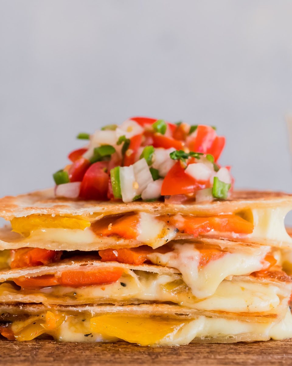 closeup profile view of stacked cheesy veggie quesadillas with pico de gallo on top