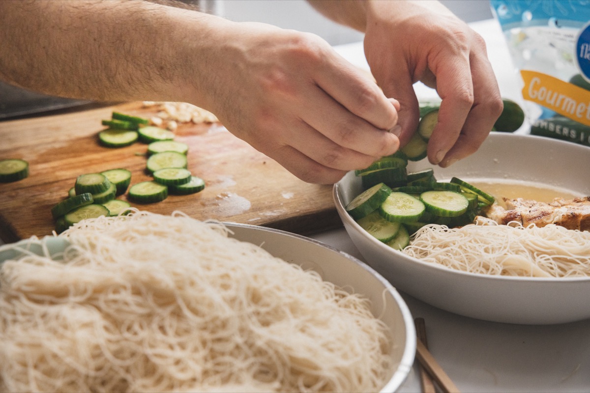 Hands serving cucumbers in noodles bowl