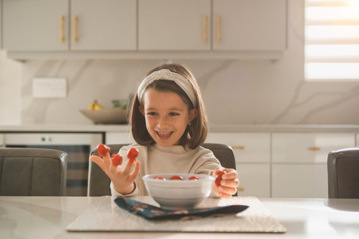 Little girl in the kitchen playing with cherry tomatoes in her hands.