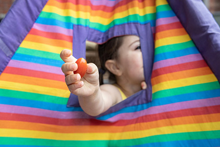 Kid playing in colorful tent with tomato