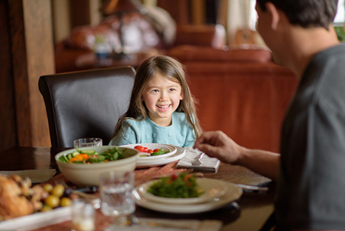 Little girl eating family meal at dinner table
