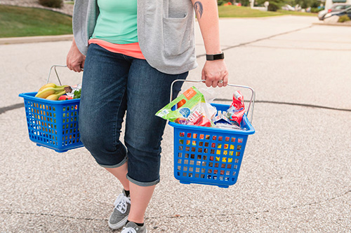 woman carrying two baskets of fresh produce in parking lot