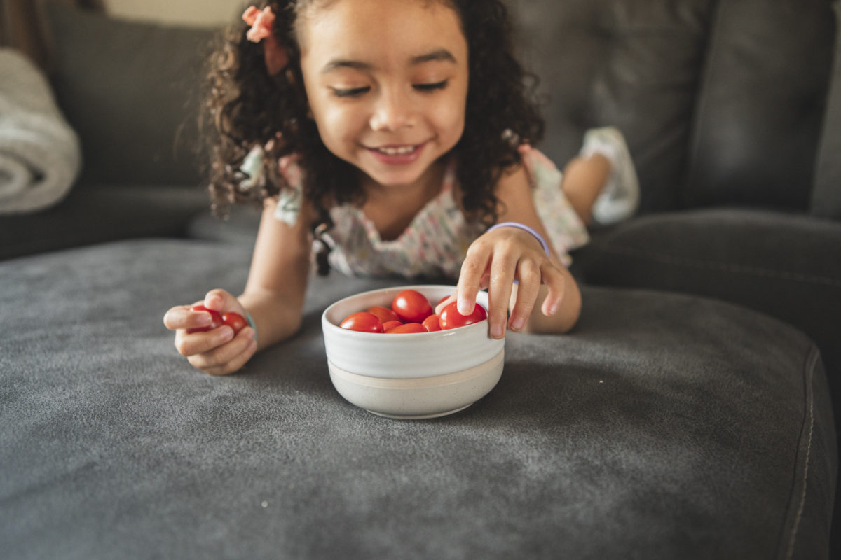 girl eating cloud 9 tomatoes from a bowl on the couch