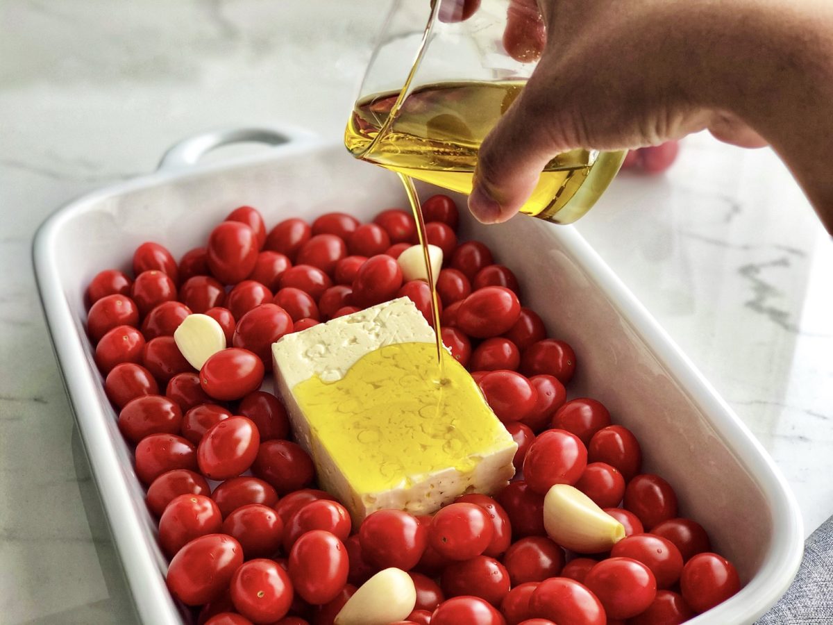 drizzling olive oil on feta surrounded by cloud 9 tomatoes in casserole dish